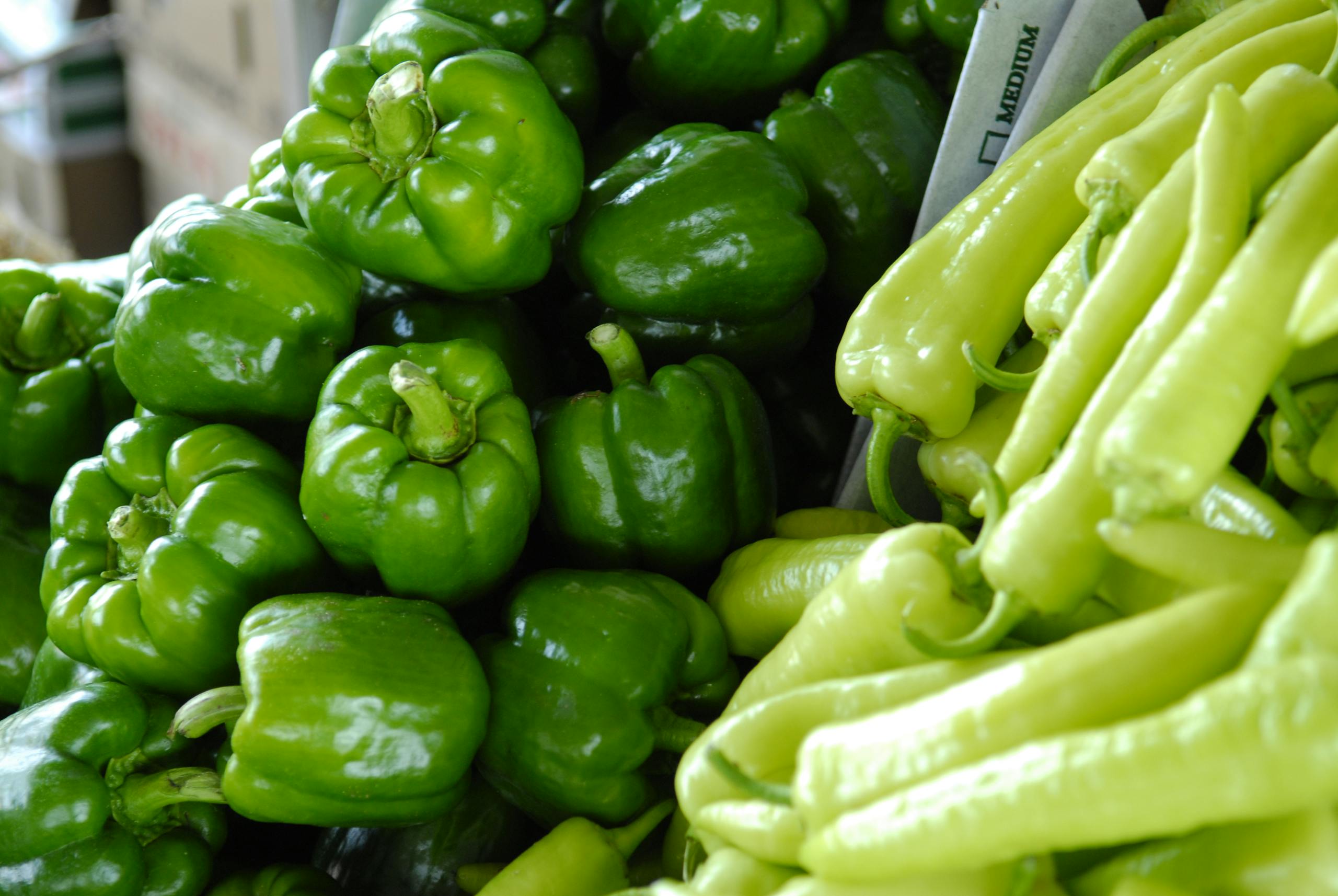 Close-up of fresh green bell peppers and chili peppers, showcasing vibrant and organic produce in a market setting.